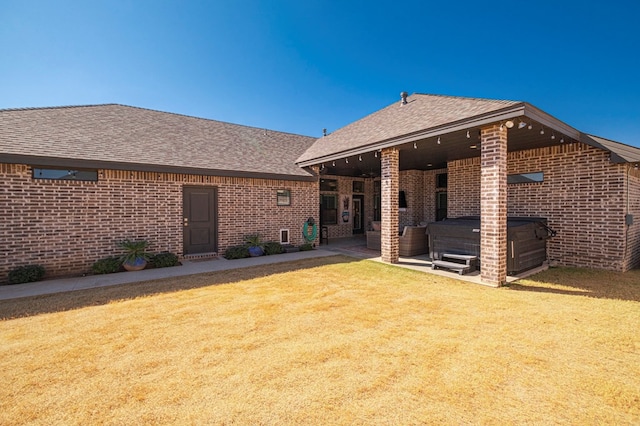 back of house featuring a hot tub, roof with shingles, a yard, a patio area, and brick siding