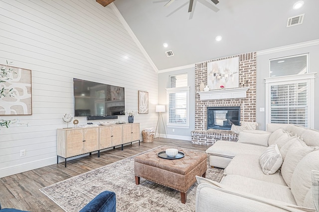 living area featuring a brick fireplace, visible vents, wood finished floors, and ornamental molding