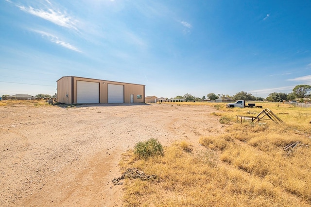 view of yard featuring a rural view, a garage, and an outbuilding