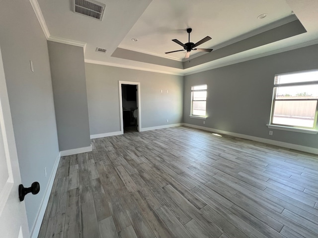 empty room with ceiling fan, ornamental molding, a tray ceiling, and light hardwood / wood-style flooring