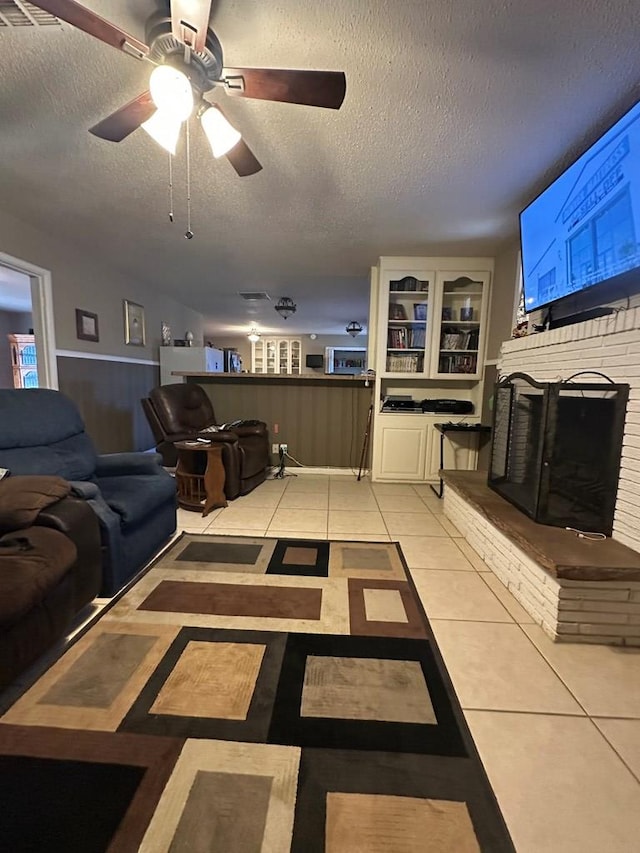 tiled living room with ceiling fan, a fireplace, and a textured ceiling