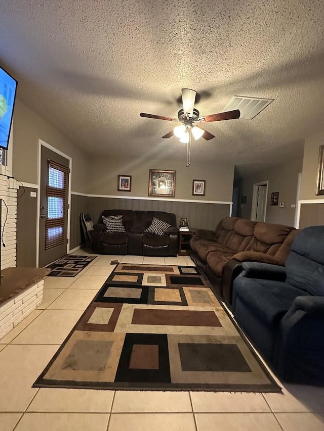 tiled living room with ceiling fan, a textured ceiling, and wood walls