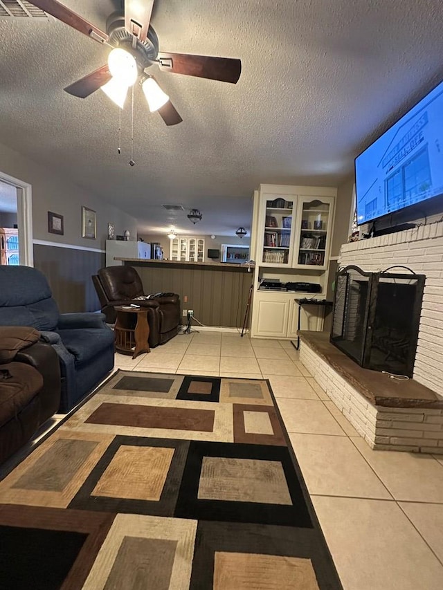 tiled living room with ceiling fan, a fireplace, and a textured ceiling