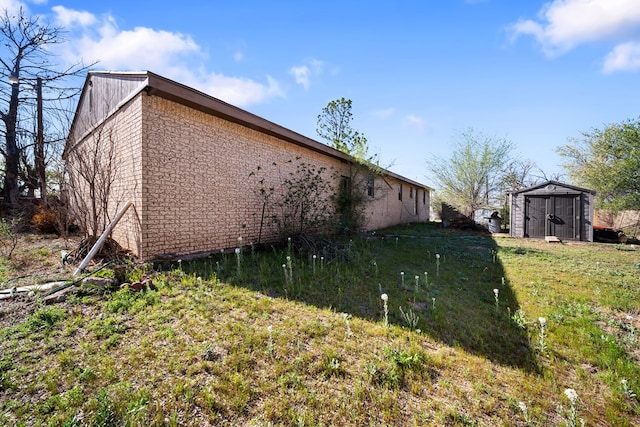 view of side of home with an outbuilding, brick siding, a lawn, and a shed