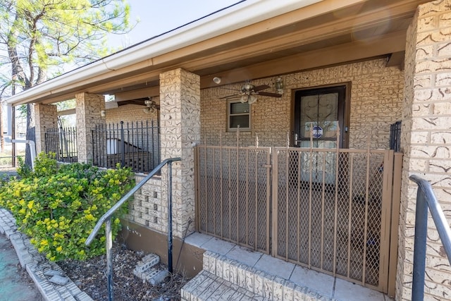 doorway to property with covered porch, brick siding, fence, and a ceiling fan