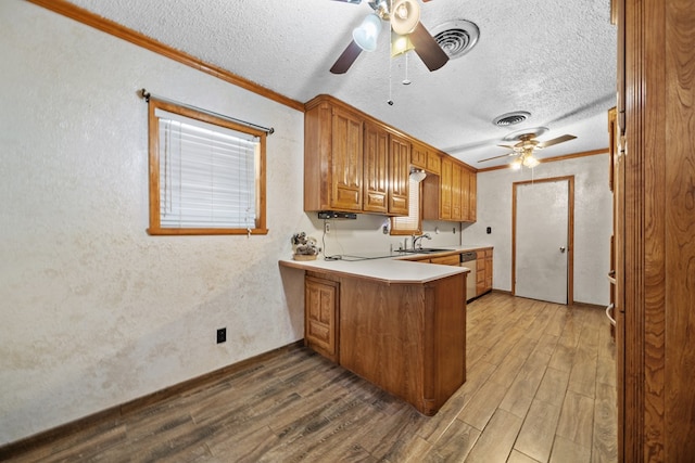 kitchen with brown cabinets, wood finished floors, a peninsula, crown molding, and stainless steel dishwasher