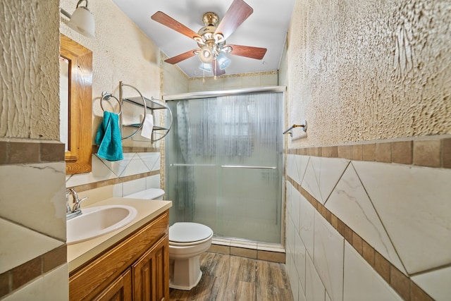 bathroom featuring toilet, a stall shower, wood finished floors, and tile walls