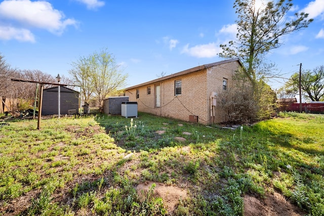 back of house featuring an outbuilding, a shed, brick siding, and central air condition unit