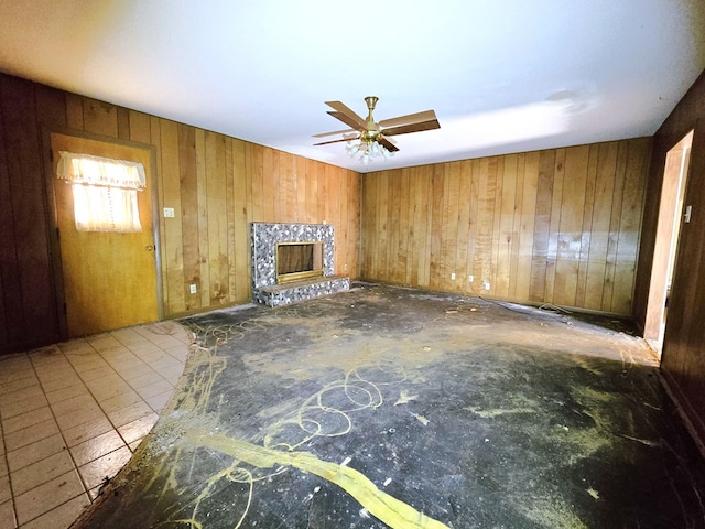 unfurnished living room featuring a fireplace with raised hearth, a ceiling fan, and wooden walls