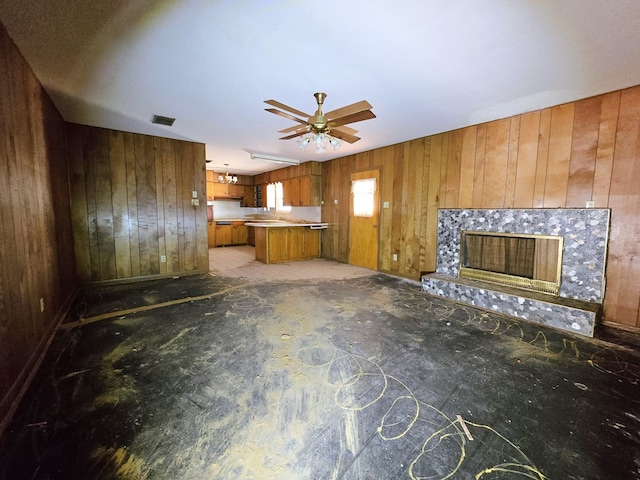 unfurnished living room featuring a ceiling fan, a premium fireplace, visible vents, and wooden walls