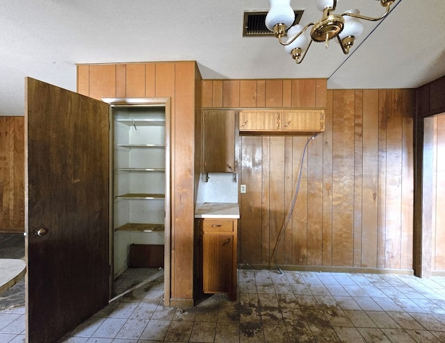 kitchen with brown cabinets, light countertops, visible vents, an inviting chandelier, and wood walls