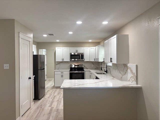 2612 Cimmaron Ave, Midland, TX 79705 - kitchen featuring stainless steel appliances, a peninsula, light stone counters, light wood-type flooring, and tasteful backsplash