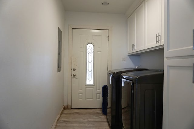 washroom with cabinets, electric panel, washer and clothes dryer, and light hardwood / wood-style flooring