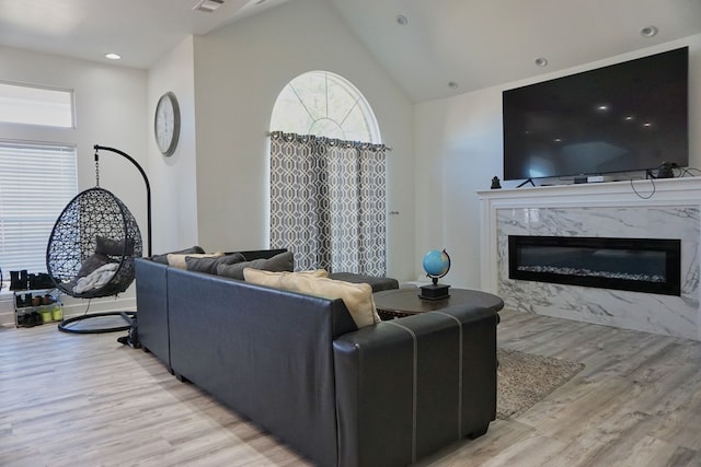 living room featuring plenty of natural light, a premium fireplace, high vaulted ceiling, and light hardwood / wood-style flooring