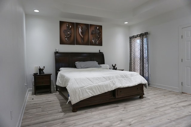 bedroom with light wood-type flooring and a tray ceiling