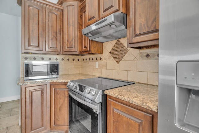 kitchen with baseboards, appliances with stainless steel finishes, under cabinet range hood, light stone countertops, and backsplash