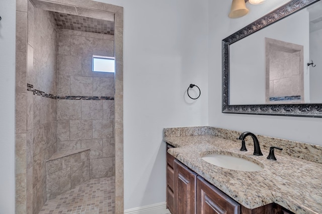 full bath featuring tiled shower, vanity, baseboards, and visible vents
