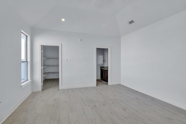 unfurnished bedroom featuring a spacious closet, visible vents, lofted ceiling, light wood finished floors, and baseboards