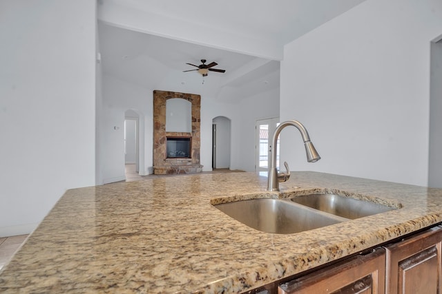 kitchen with arched walkways, a sink, ceiling fan, beamed ceiling, and light stone countertops
