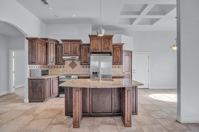 kitchen featuring a towering ceiling, under cabinet range hood, decorative backsplash, arched walkways, and appliances with stainless steel finishes