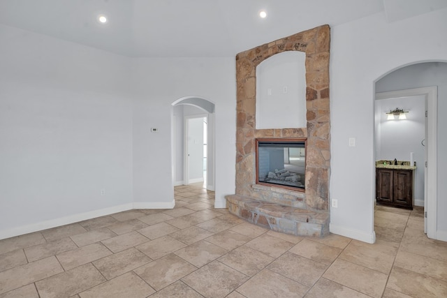 unfurnished living room with a stone fireplace, recessed lighting, arched walkways, and baseboards