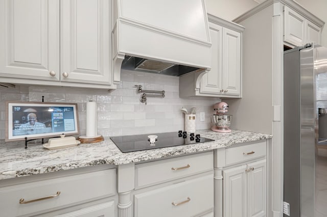 kitchen with black electric stovetop, white cabinetry, stainless steel fridge with ice dispenser, decorative backsplash, and custom range hood