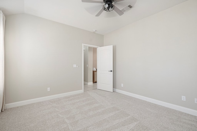 empty room with lofted ceiling, light colored carpet, a ceiling fan, baseboards, and visible vents