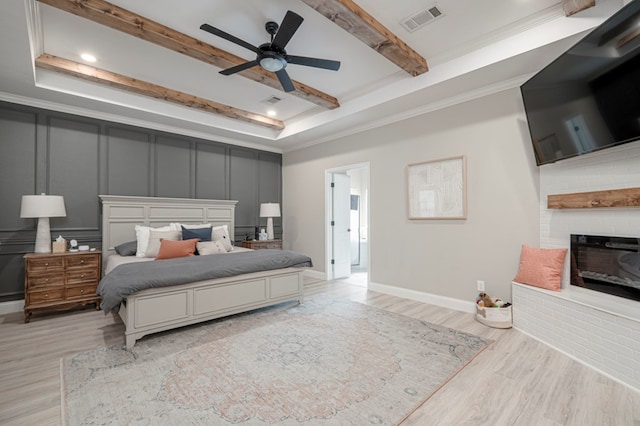 bedroom featuring a decorative wall, wood finished floors, visible vents, a brick fireplace, and beam ceiling