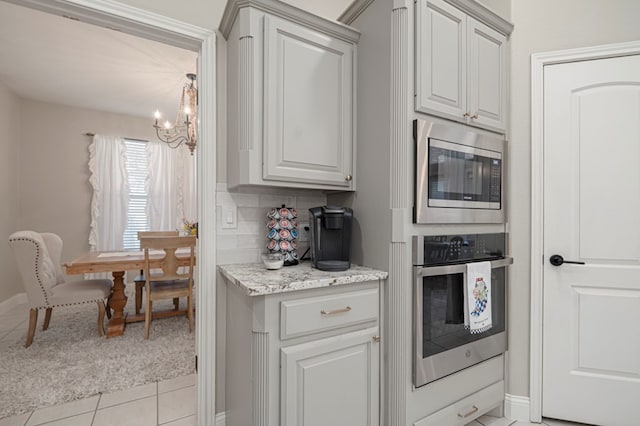 kitchen featuring a notable chandelier, light tile patterned floors, tasteful backsplash, light colored carpet, and appliances with stainless steel finishes