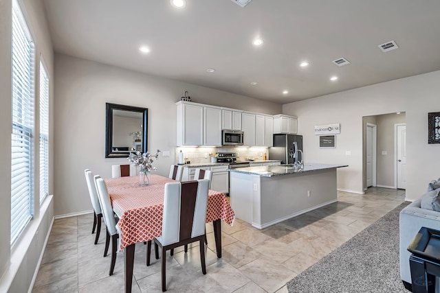 kitchen with decorative backsplash, light stone counters, stainless steel appliances, white cabinetry, and an island with sink