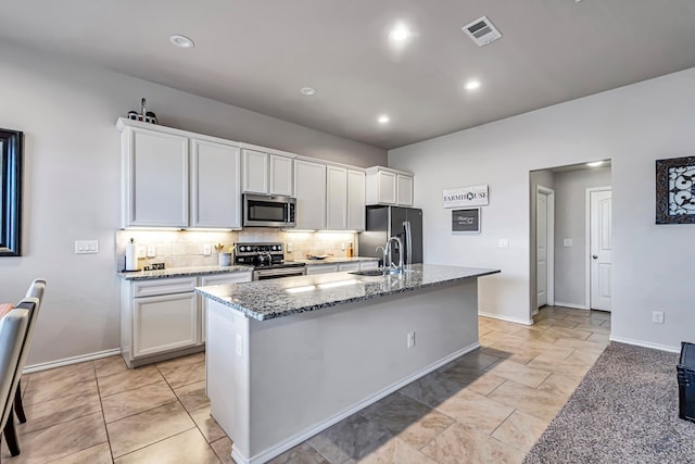 kitchen featuring light stone counters, backsplash, an island with sink, white cabinets, and appliances with stainless steel finishes