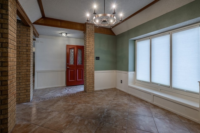 foyer featuring a wainscoted wall, a textured ceiling, and ornate columns