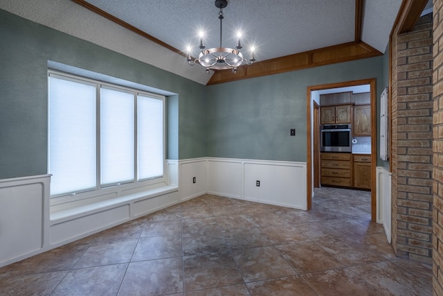 empty room with wainscoting, an inviting chandelier, a textured ceiling, and vaulted ceiling