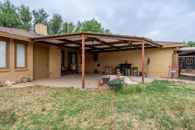 back of property featuring a chimney, brick siding, an attached carport, and a patio area