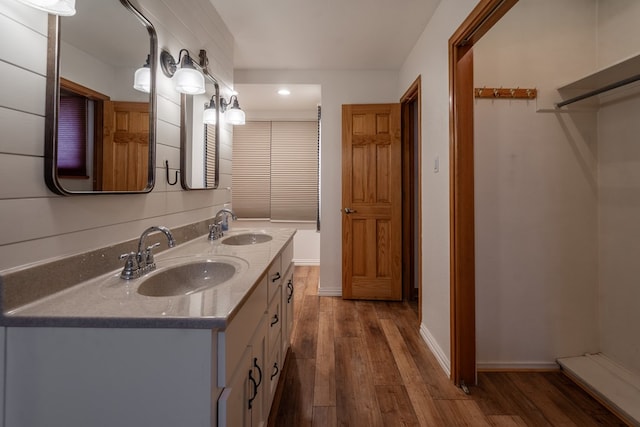 bathroom featuring baseboards, wood finished floors, double vanity, and a sink