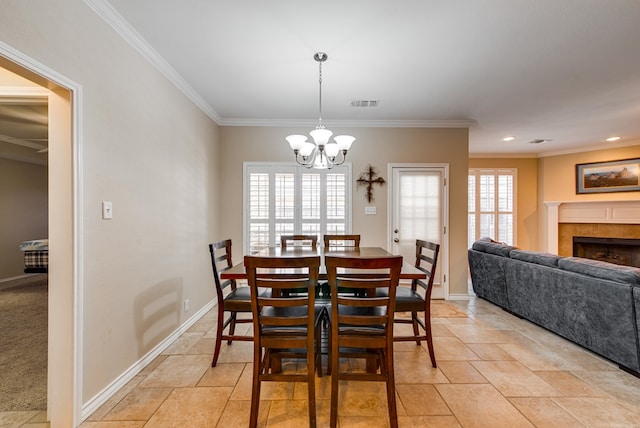 dining space with baseboards, a chandelier, ornamental molding, a tile fireplace, and light stone finish floors