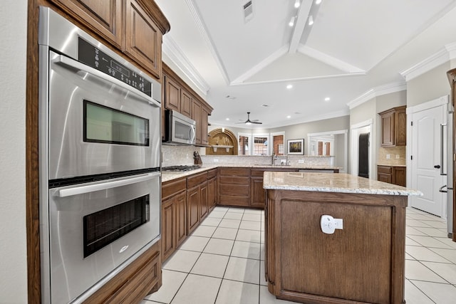 5703 Devlin Pl, Midland, TX 79707 - kitchen featuring appliances with stainless steel finishes, light tile patterned floors, backsplash, a center island, and light stone countertops