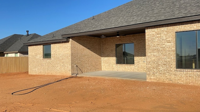 rear view of property featuring a ceiling fan, fence, roof with shingles, brick siding, and a patio area