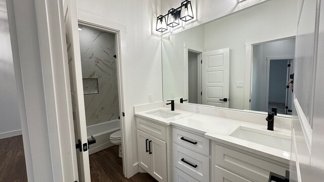 full bath featuring double vanity, wood finish floors, toilet, and a sink