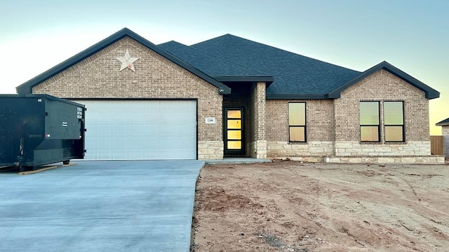 ranch-style house with roof with shingles, concrete driveway, stone siding, a garage, and brick siding