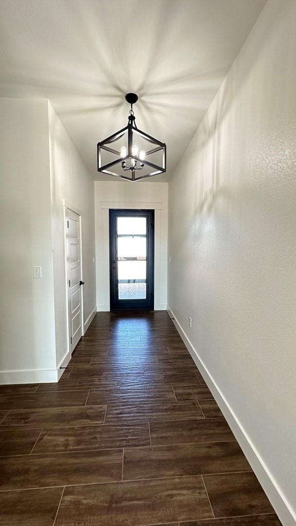 entryway with baseboards, dark wood-type flooring, and an inviting chandelier