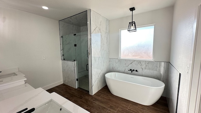 full bathroom featuring a marble finish shower, tile walls, wood tiled floor, a freestanding tub, and vanity