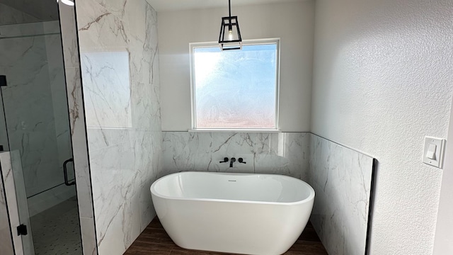 bathroom featuring a marble finish shower, a textured wall, wood finished floors, a soaking tub, and tile walls