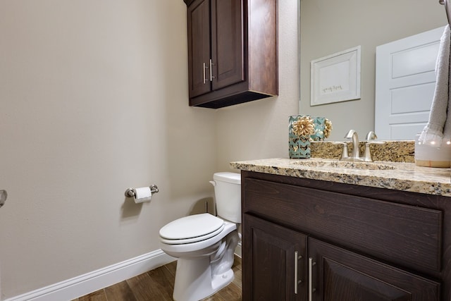 half bathroom with baseboards, toilet, wood finished floors, and vanity