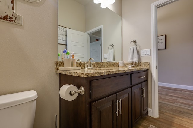 bathroom featuring wood finished floors, baseboards, vanity, and toilet