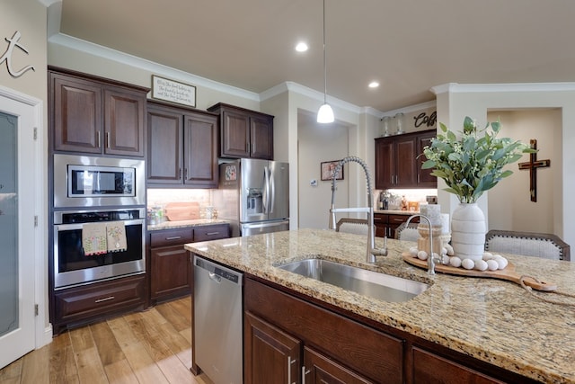 kitchen with stainless steel appliances, a sink, ornamental molding, light wood-style floors, and light stone countertops