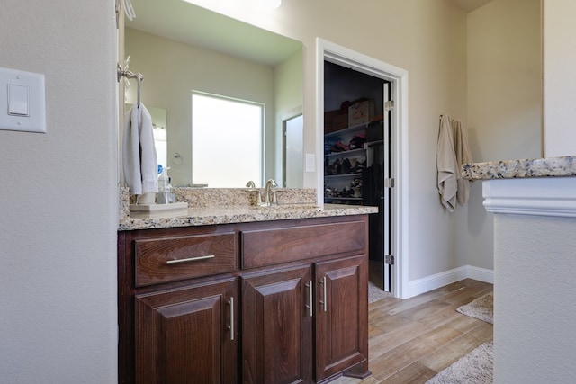 full bathroom featuring vanity, wood finished floors, a walk in closet, and baseboards