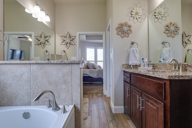 ensuite bathroom featuring wood-type flooring, a tub to relax in, vanity, baseboards, and ceiling fan