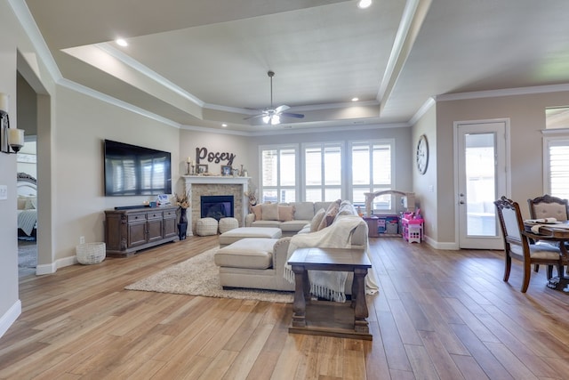 living area featuring a tray ceiling, ceiling fan, light wood-type flooring, crown molding, and baseboards