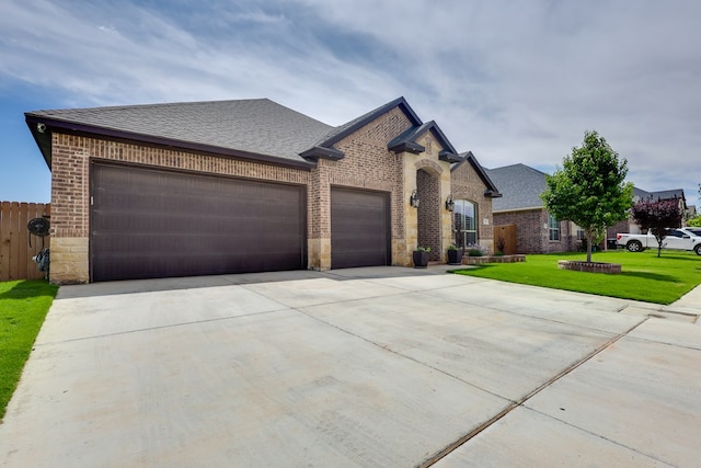 french country inspired facade featuring a garage, driveway, brick siding, and roof with shingles